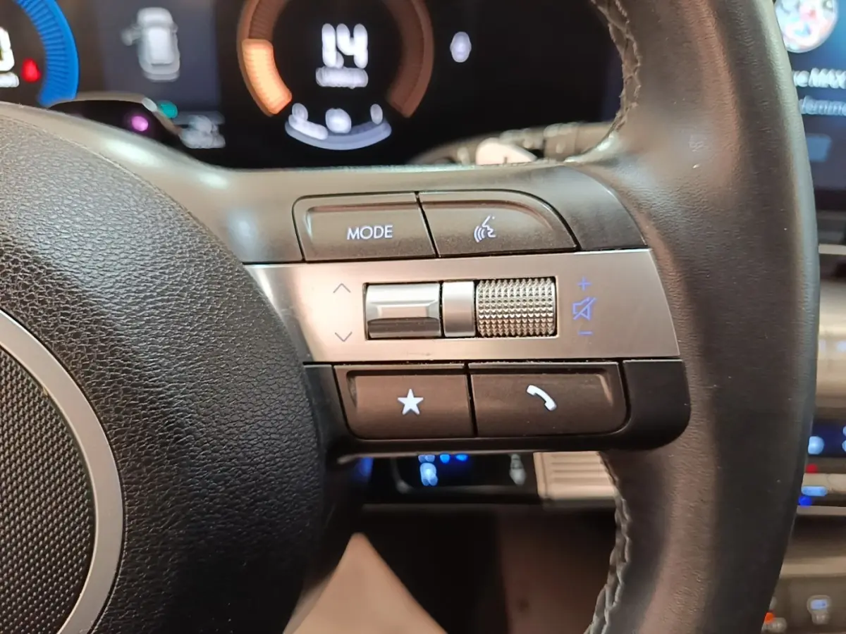 Gros plan sur les commandes multifonctions en cuir du volant du Hyundai Kona 1.6 Hybrid 2024, avec affichage numérique en arrière-plan.