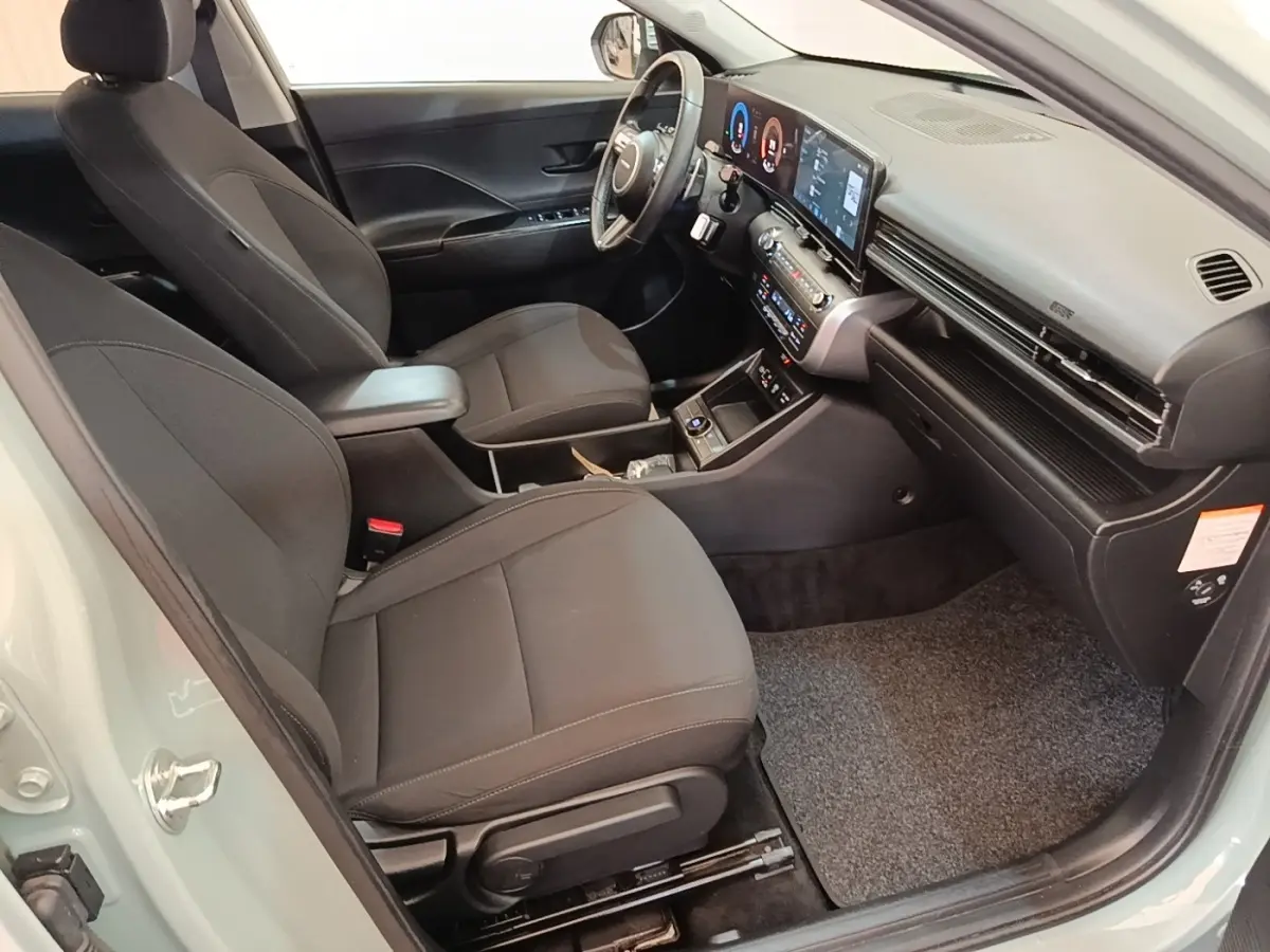 Vue intérieure côté conducteur de la Hyundai KONA 2024, sièges noirs et tableau de bord avec écran tactile large.