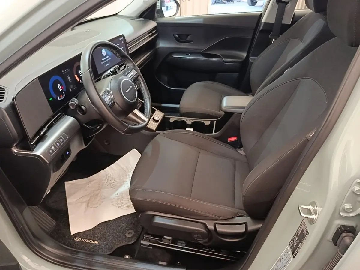 Vue intérieure côté conducteur du Hyundai Kona 2024, sièges noirs et tableau de bord avec écran tactile large.