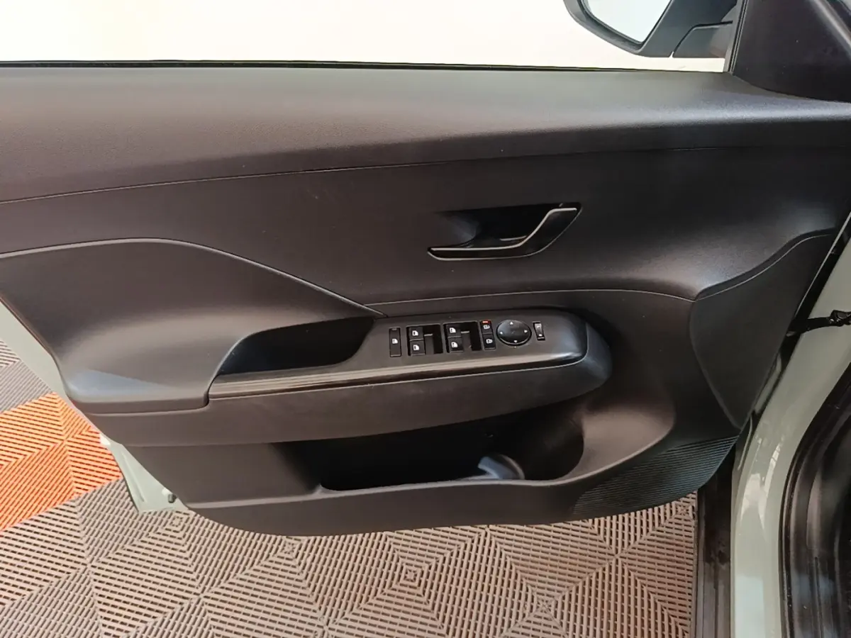Vue intérieure de la porte avant gauche du Hyundai Kona 2024 vert, avec commandes électriques des vitres et rétroviseurs.