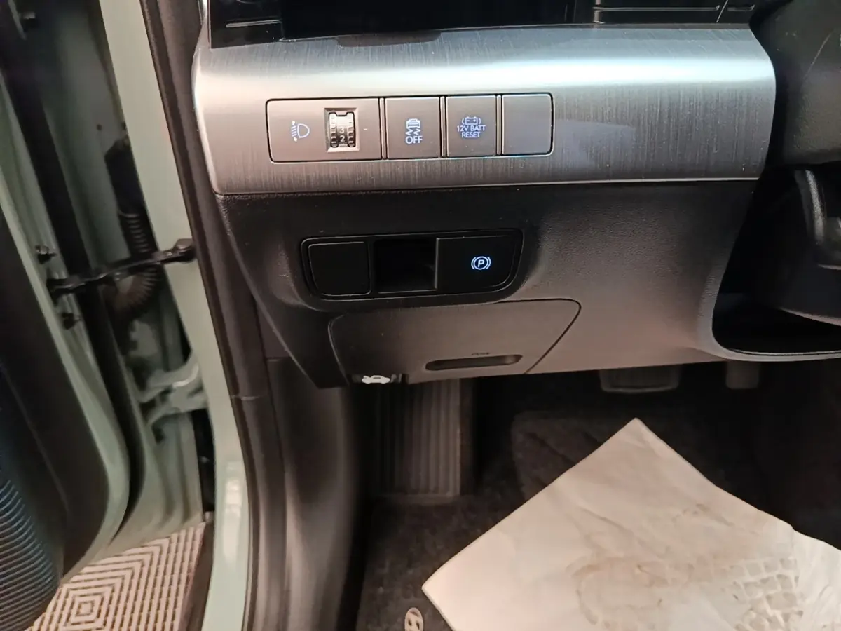 Détail des commandes sous le tableau de bord côté gauche du Hyundai Kona vert 2024, avec bouton frein à main électrique.