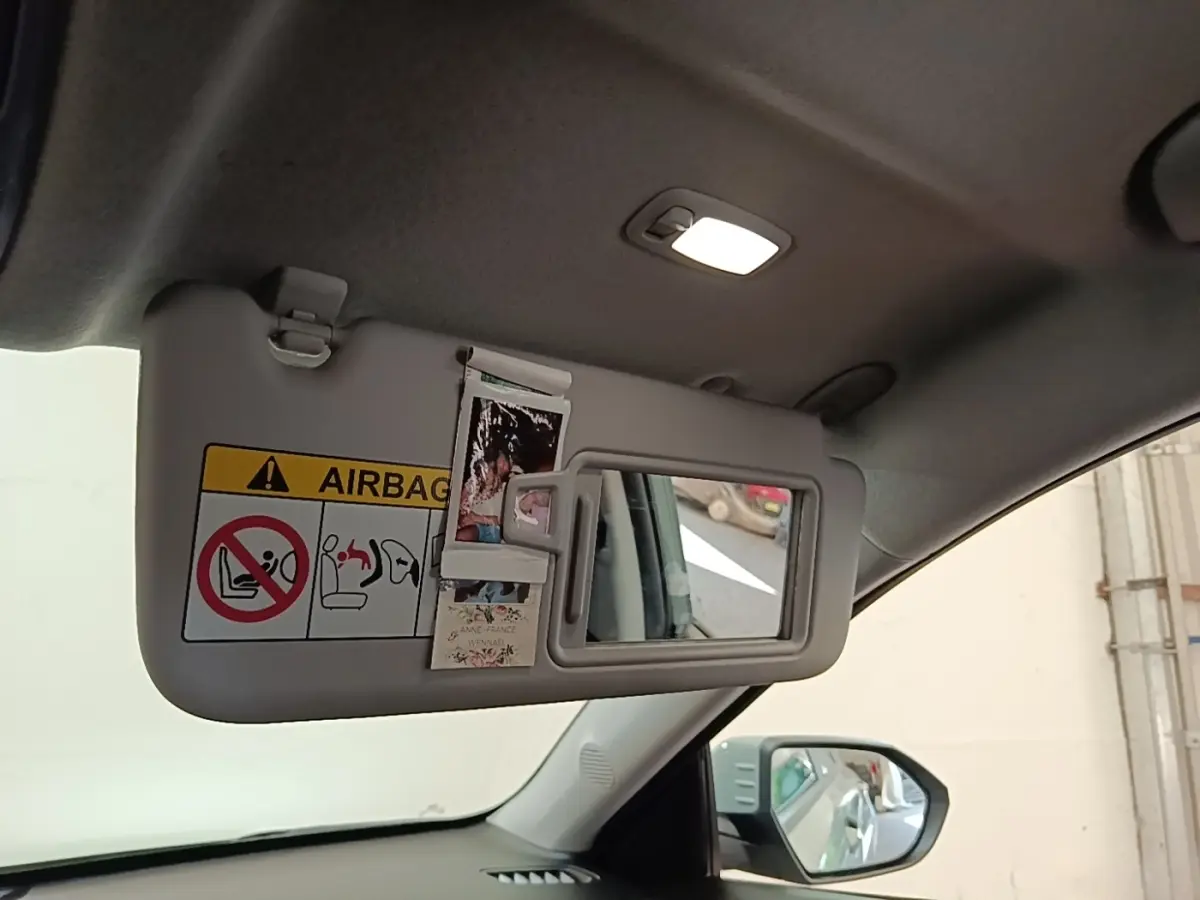 Détail intérieur du pare-soleil côté conducteur avec miroir et autocollants dans un Hyundai Kona vert 2024.