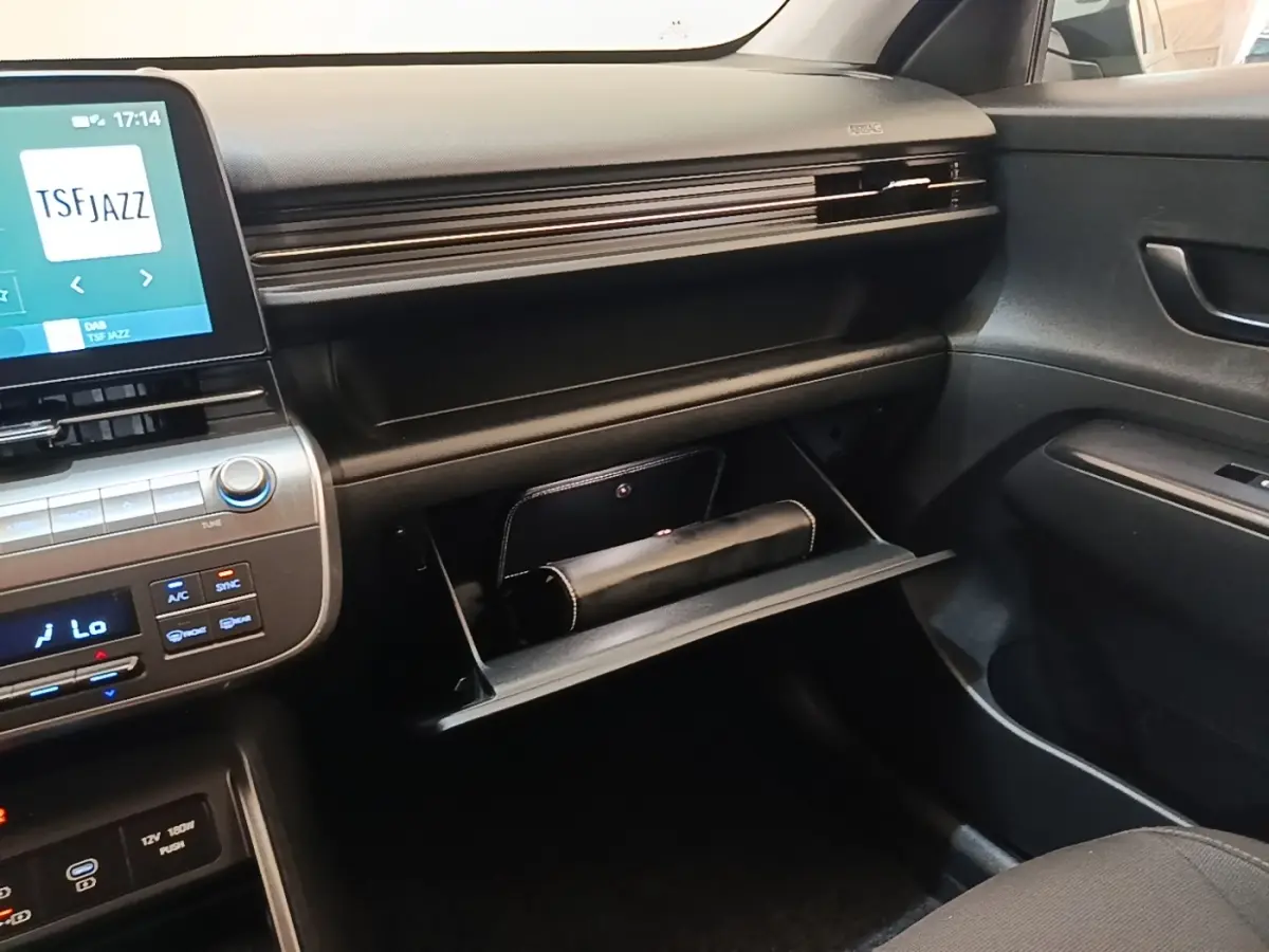 Intérieur de la Hyundai Kona 1.6 Hybrid 2024, vue côté passager sur la boîte à gants ouverte et tableau de bord noir.