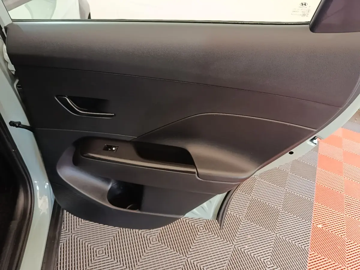 Porte arrière droite ouverte du Hyundai Kona vert, montrant le panneau intérieur noir avec poignée et commande vitre.