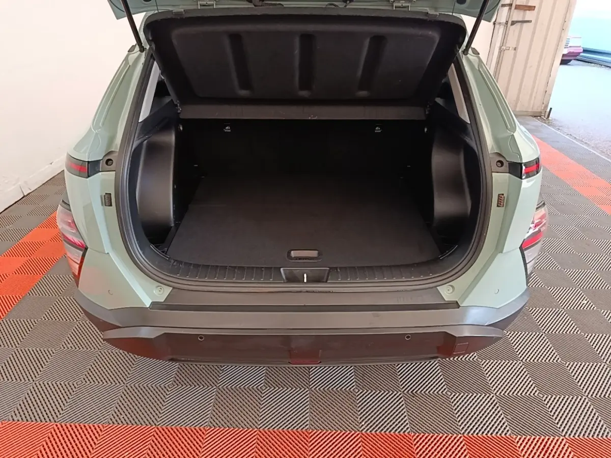 Vue arrière du coffre ouvert d'un Hyundai Kona 2024 vert, montrant l'espace de rangement vide et le pare-chocs noir.