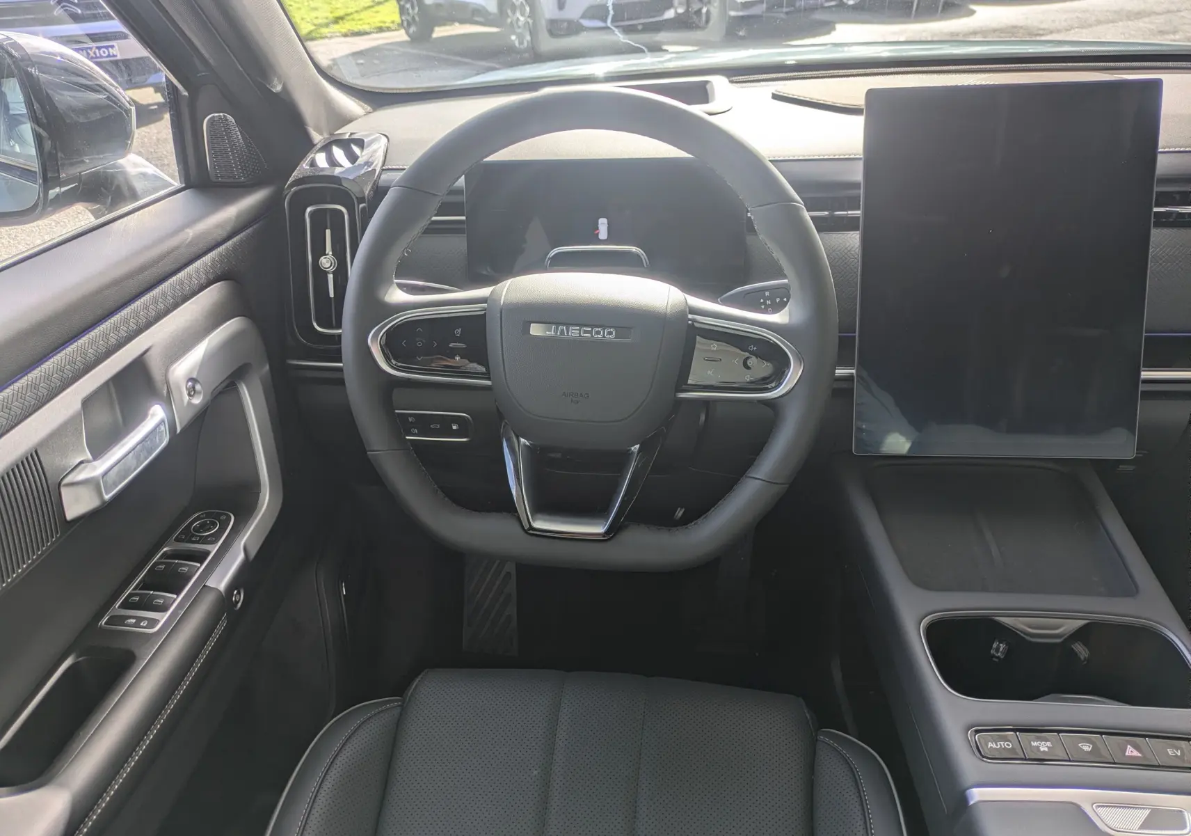 Vue intérieure centrée sur le volant JAECOO avec tableau de bord numérique et grand écran tactile vertical, ambiance noire.