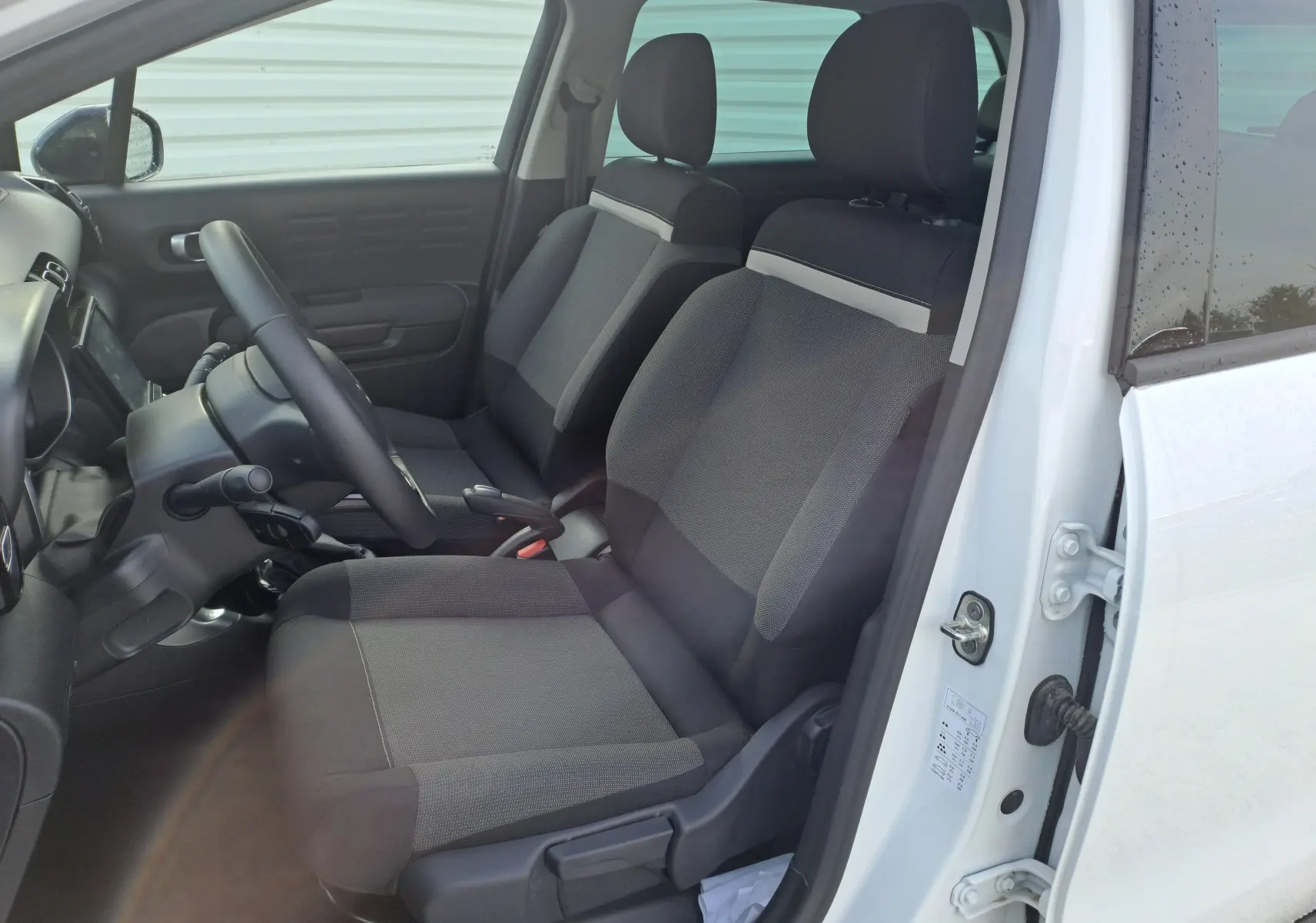 Vue intérieure côté conducteur d'une Citroën C3 Aircross blanc banquise, sièges tissu gris et tableau de bord visible.