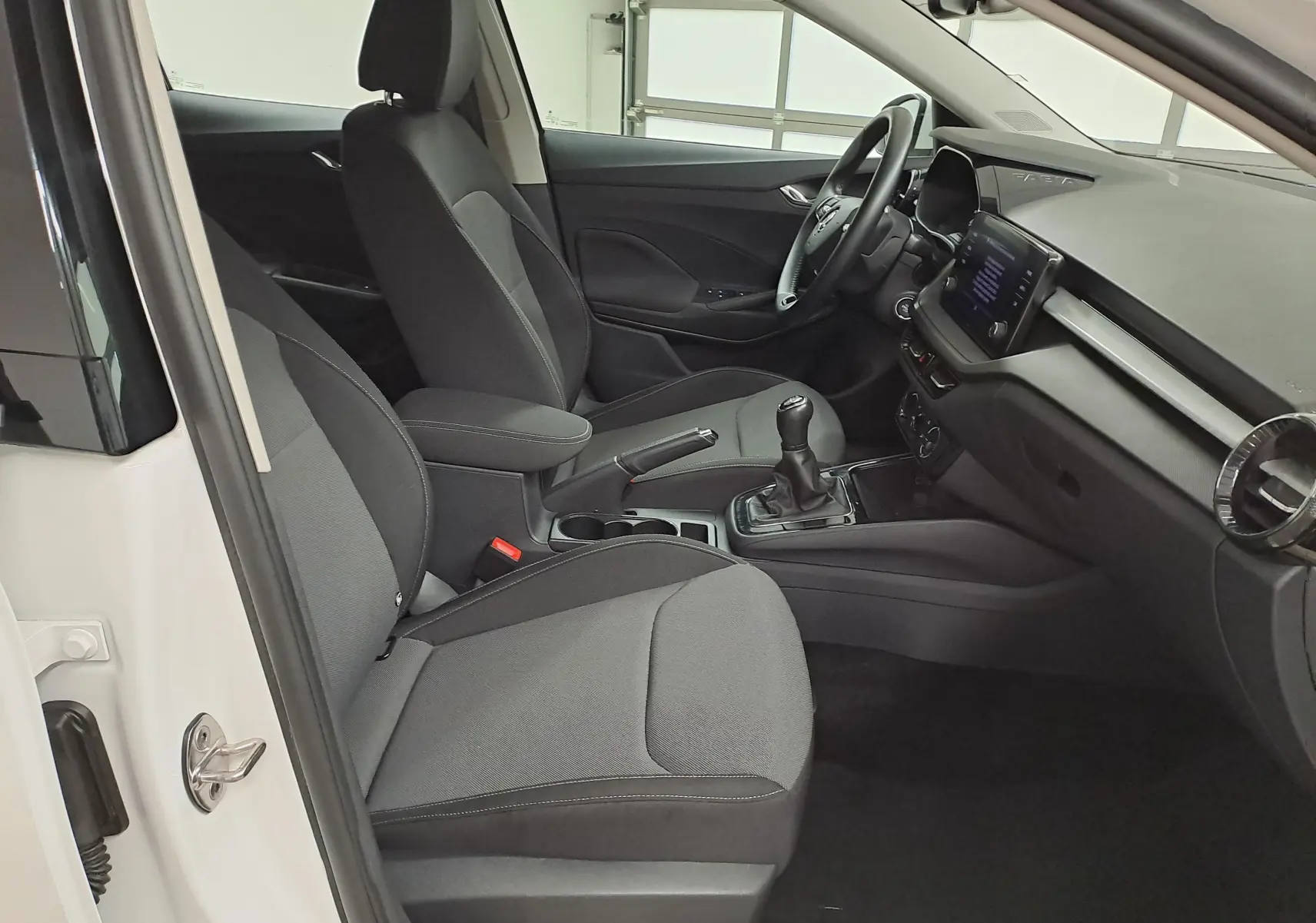 Intérieur côté conducteur d'une Skoda Fabia blanche 2023, avec sièges gris et tableau de bord moderne à écran tactile.