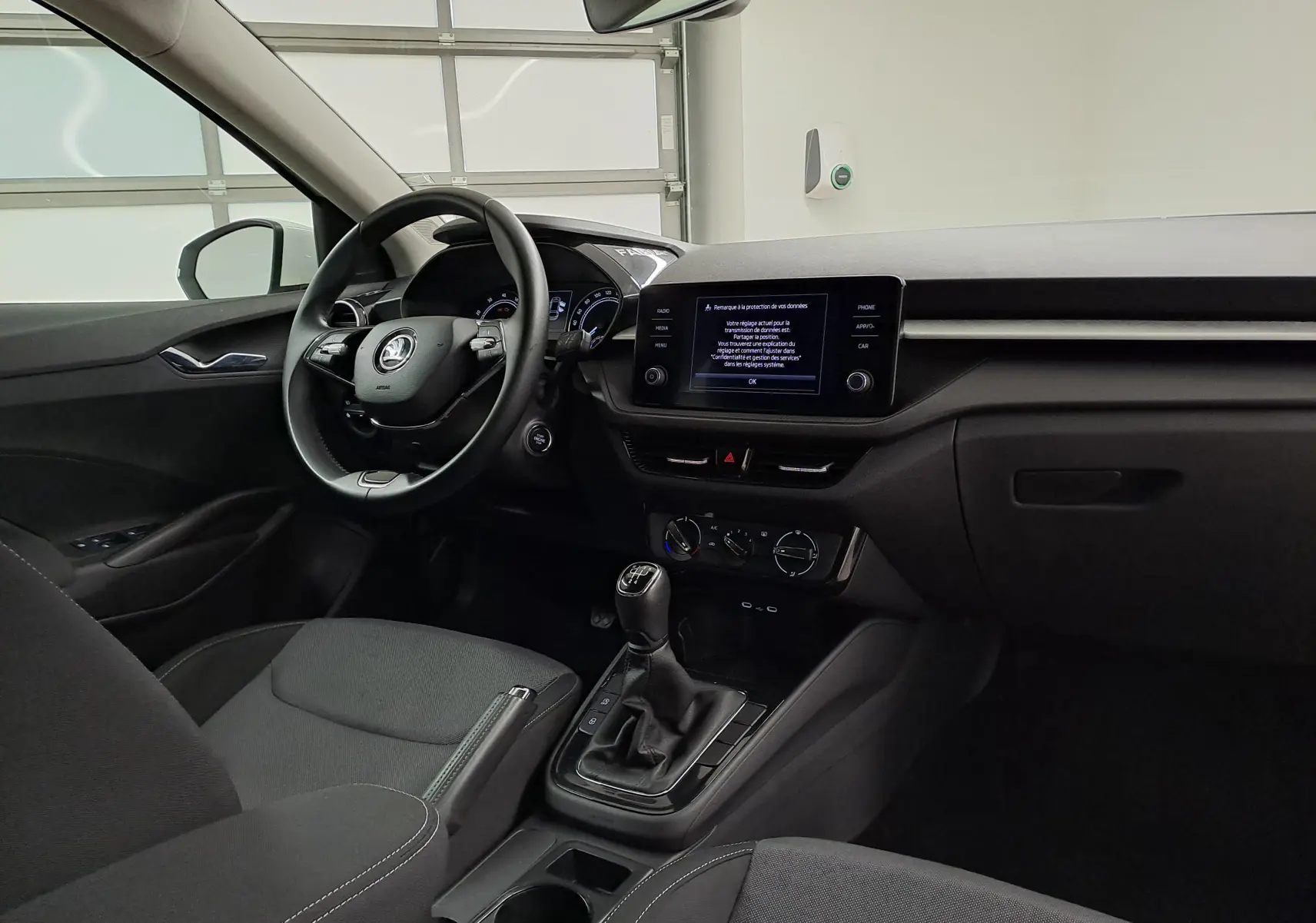 Vue intérieure côté conducteur de la Skoda Fabia 2023 blanche, avec tableau de bord moderne et boîte manuelle visible.