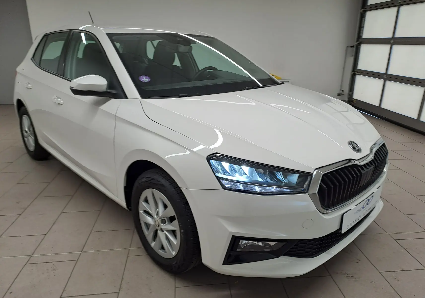 Vue 3/4 avant droite d'une Skoda Fabia 2023 blanc candy avec phares allumés et calandre noire distinctive.