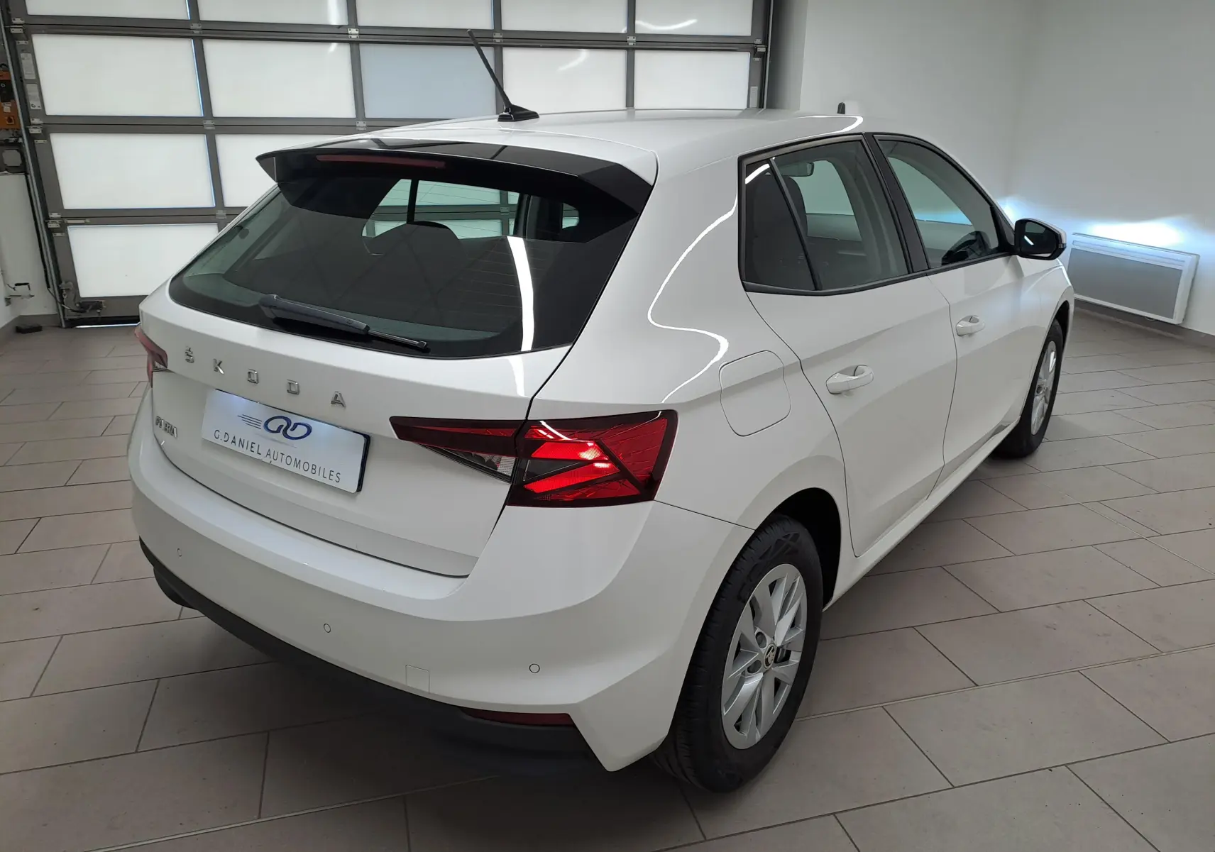 Vue 3/4 arrière droite d'une Skoda Fabia 2023 blanche Candy avec feux arrière allumés dans un garage.