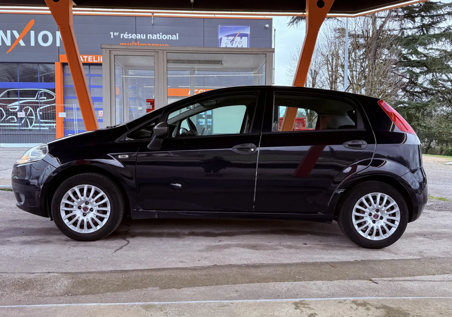 Profil côté gauche d'une Fiat Punto noire de 2009, avec jantes argentées et carrosserie compacte sous un abri.