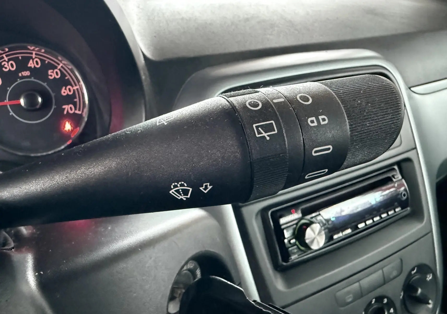 Gros plan sur la commande d’essuie-glace noire dans l’habitacle d’une Fiat Punto 2009, avec tableau de bord et autoradio en arrière-plan.