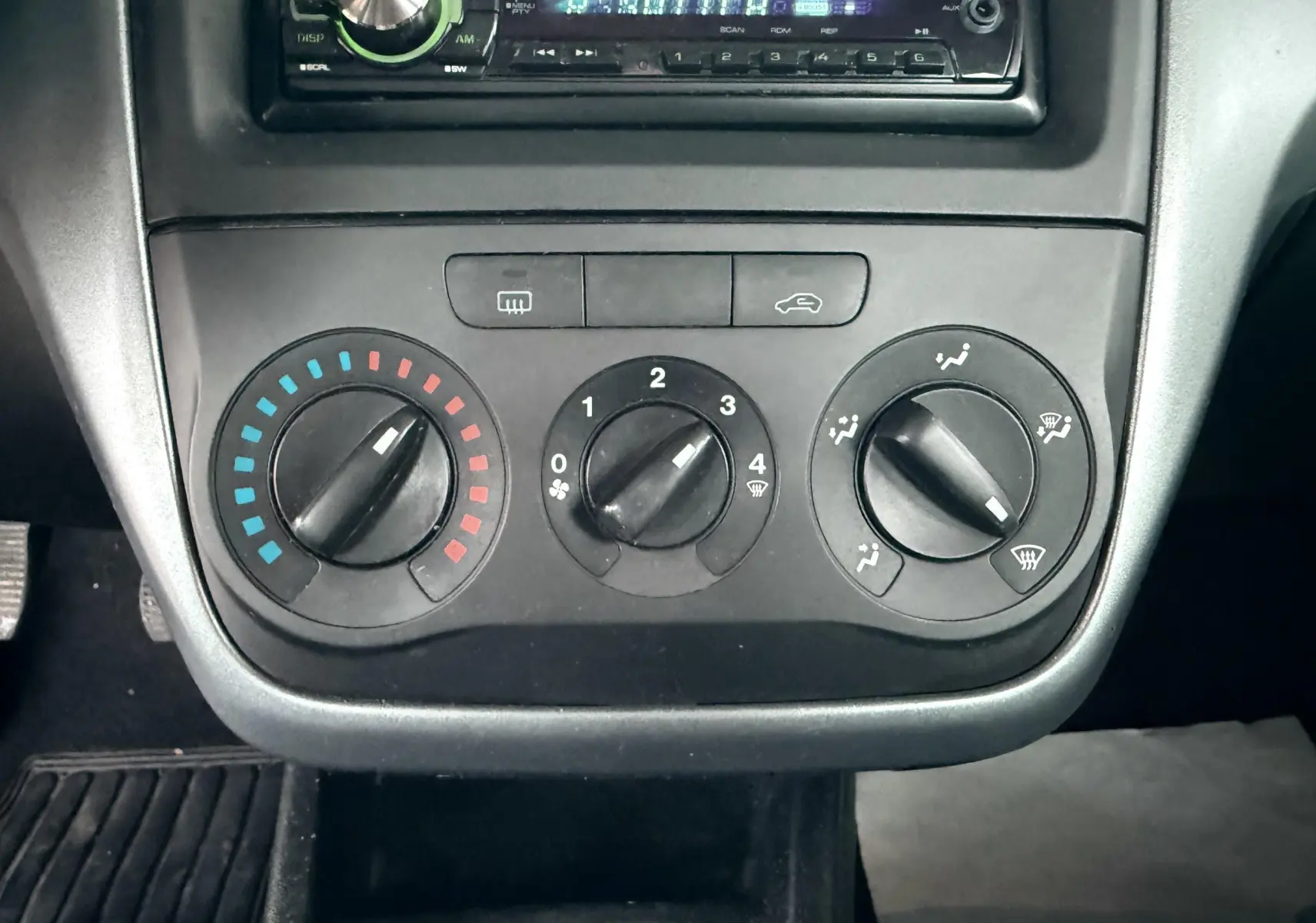 Gros plan sur les commandes de climatisation manuelles et autoradio d’une Fiat Punto noire de 2009.