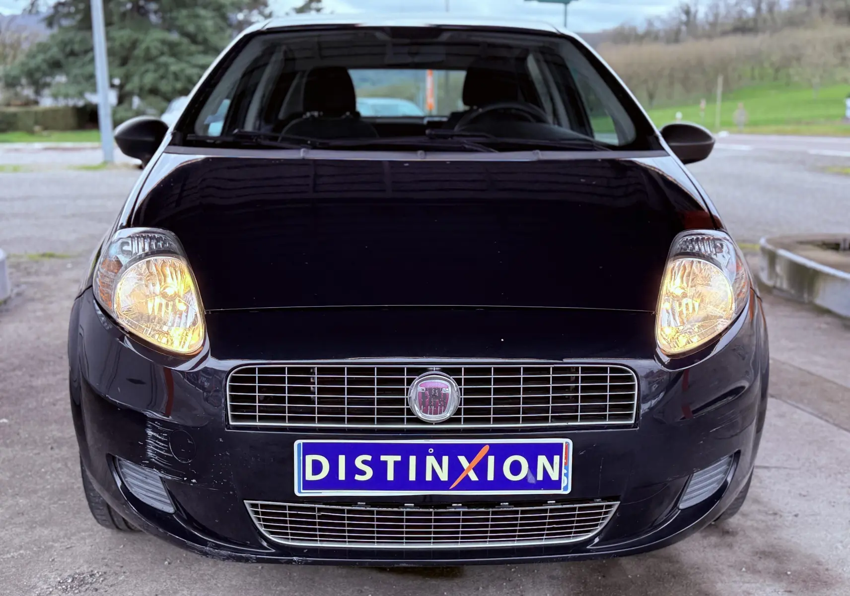 Vue avant d'une FIAT Punto noire de 2009 avec phares allumés et plaque d'immatriculation Distinxion.