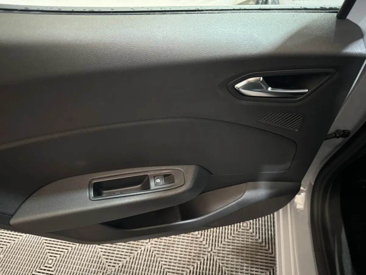 Vue rapprochée de la porte avant droite gris clair de la Renault Clio 2025 avec poignée intérieure et commande de vitre électrique.