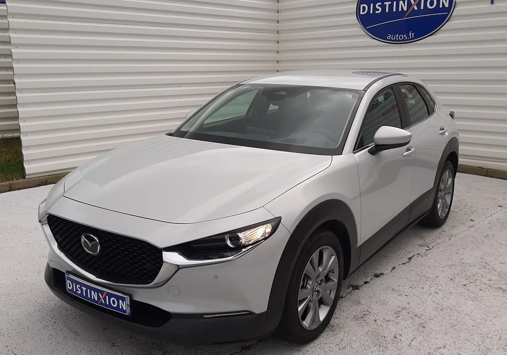 Vue 3/4 avant droite d'un Mazda CX-30 2024 blanc céramique avec calandre noire et feux LED allumés.