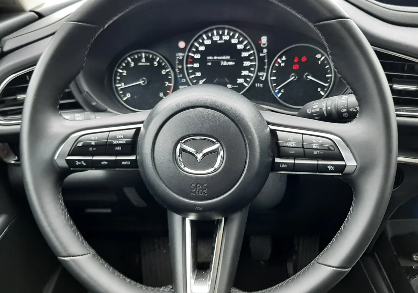 Vue frontale du volant noir de la Mazda CX-30 2024 avec commandes intégrées et tableau de bord digital.