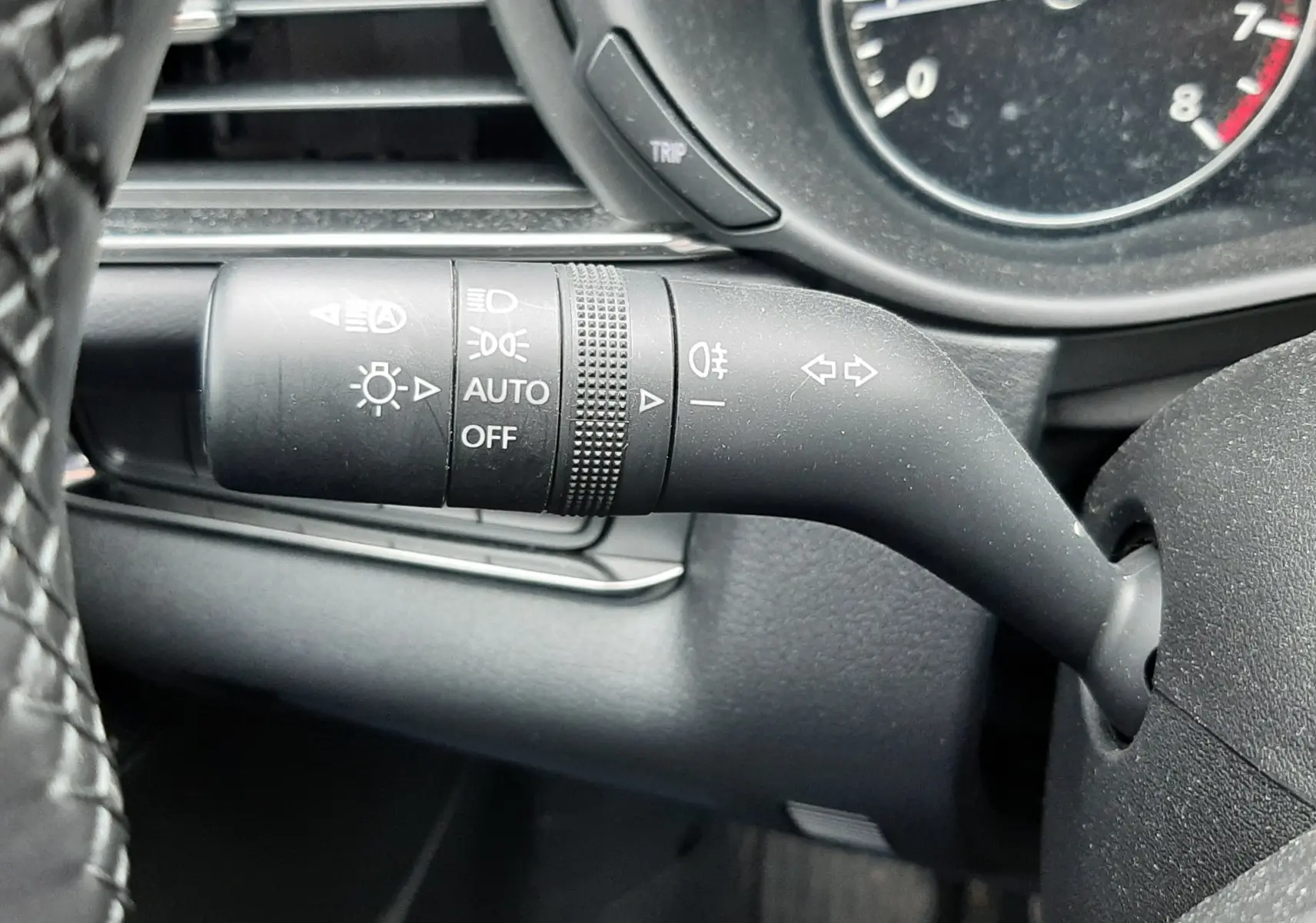 Gros plan sur la manette de clignotants noire à gauche du volant dans l’habitacle noir du Mazda CX-30 2024.