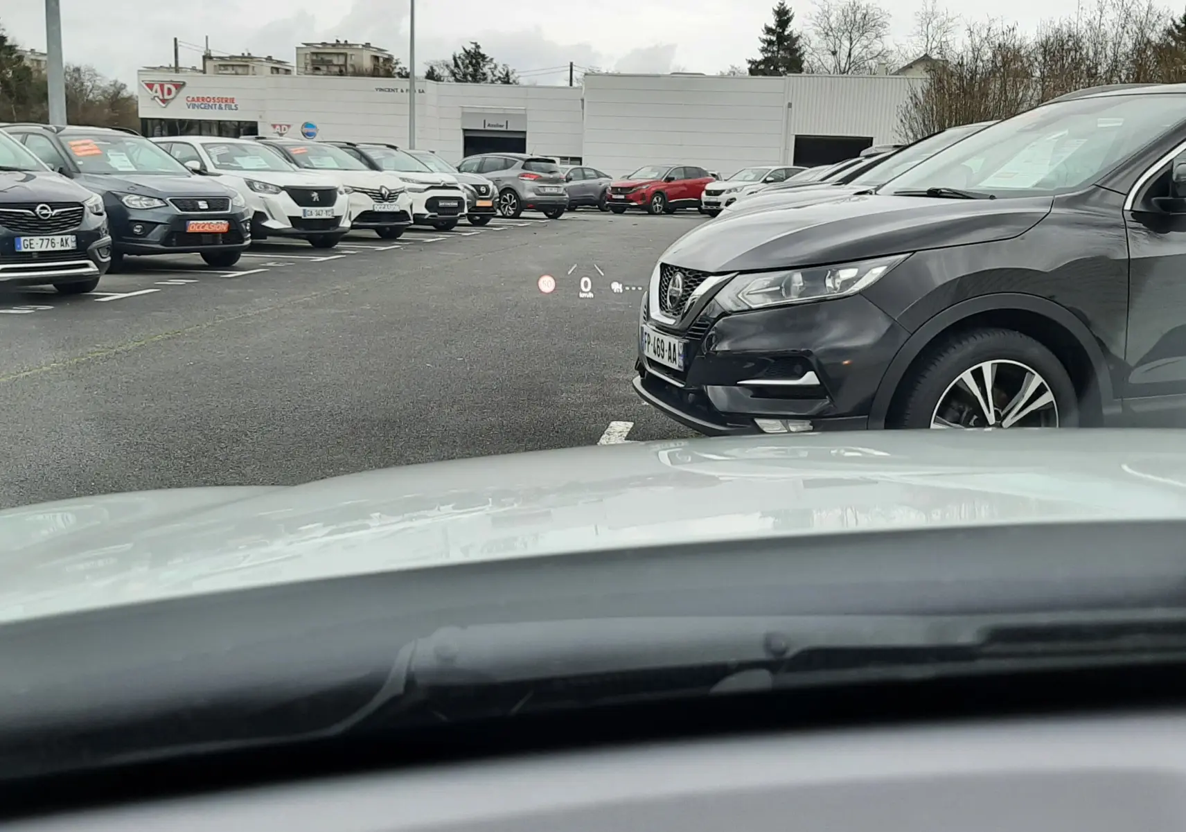 Vue depuis l'habitacle montrant le capot blanc d'une Mazda CX-30 2024 en Ceramic White sur un parking extérieur.