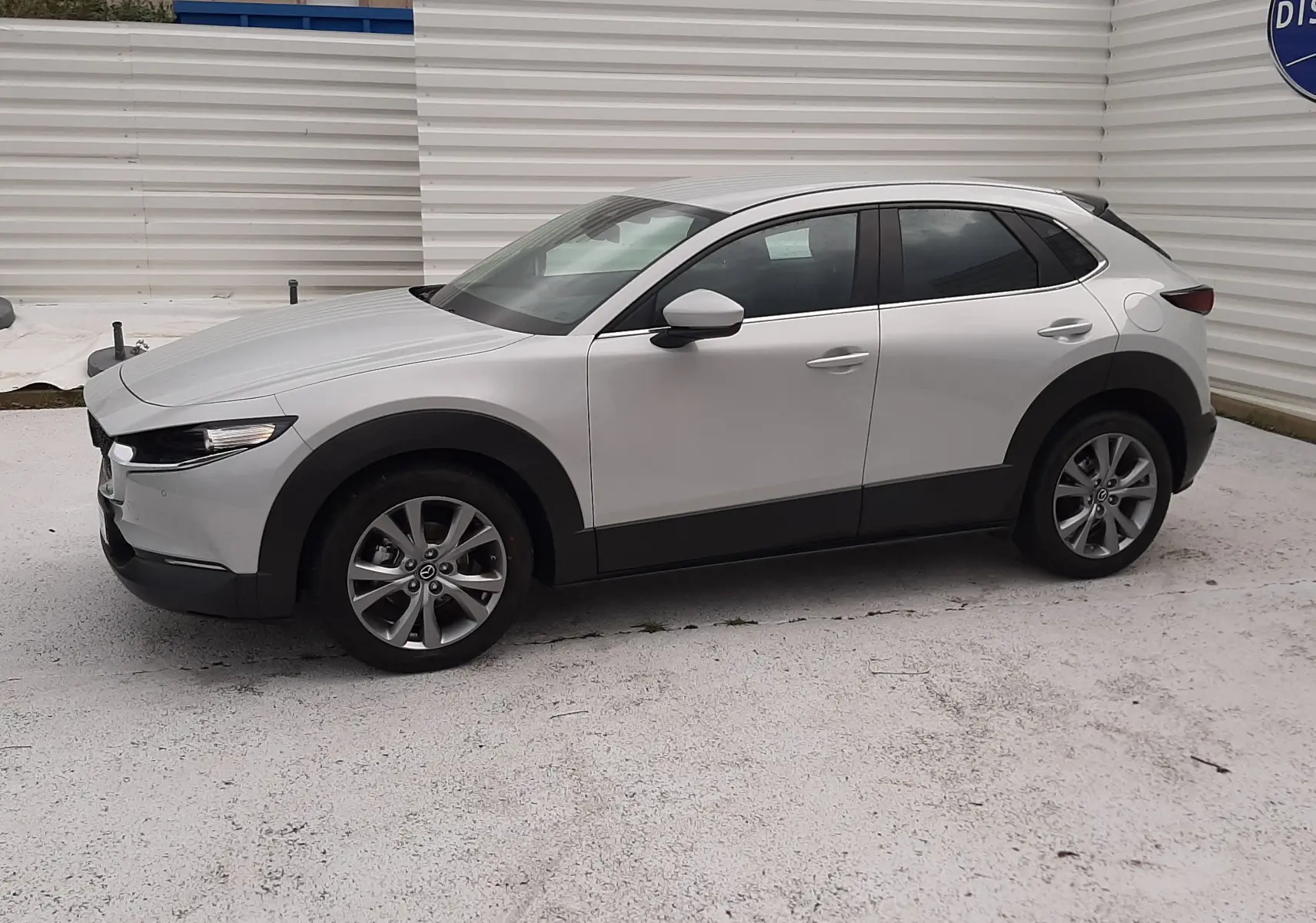 Vue de profil côté gauche d'un Mazda CX-30 2024 blanc céramique avec jantes alliage et protections noires basses.
