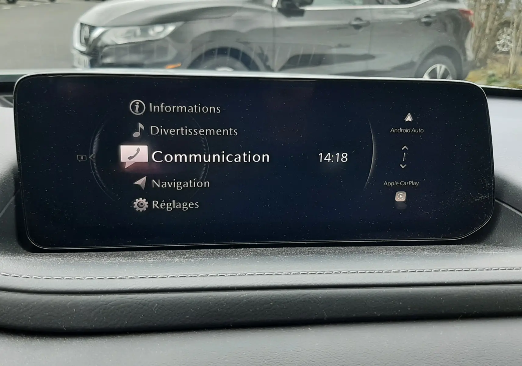 Écran central de la Mazda CX-30 2024 affichant le menu communication, vue intérieure avant avec reflet extérieur.