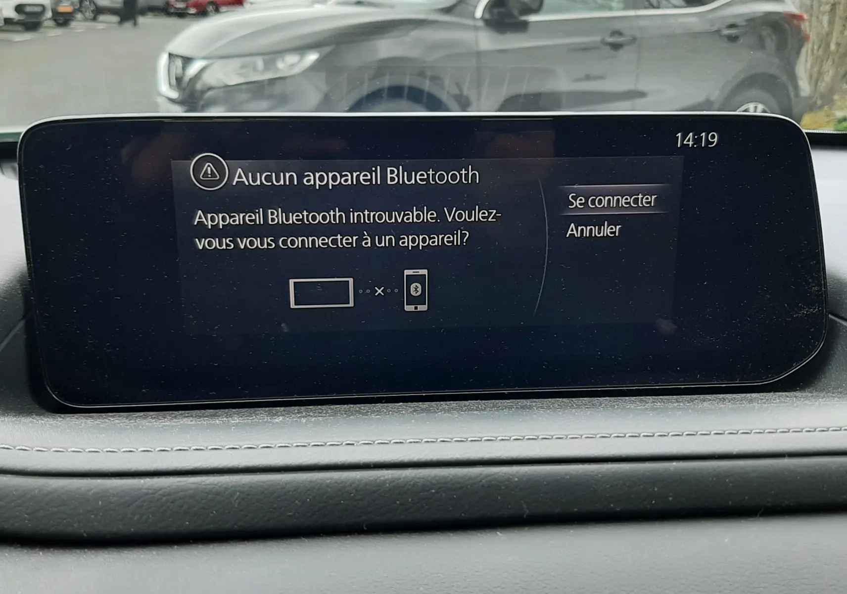 Écran central du tableau de bord du Mazda CX-30 2024 affichant un message Bluetooth, avec vue floue d’un SUV gris en arrière-plan.