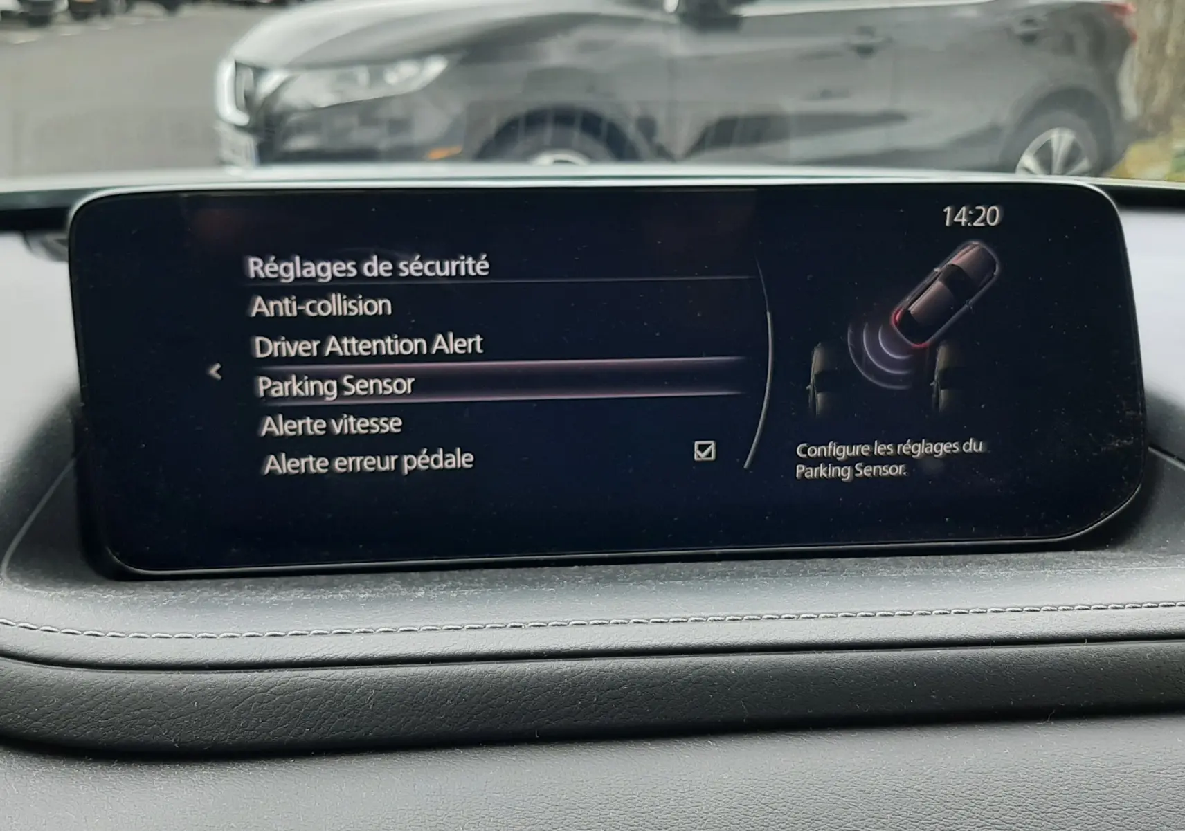 Vue intérieure du tableau de bord de la Mazda CX-30 2024, écran affichant les réglages de sécurité avec un véhicule gris en arrière-plan.