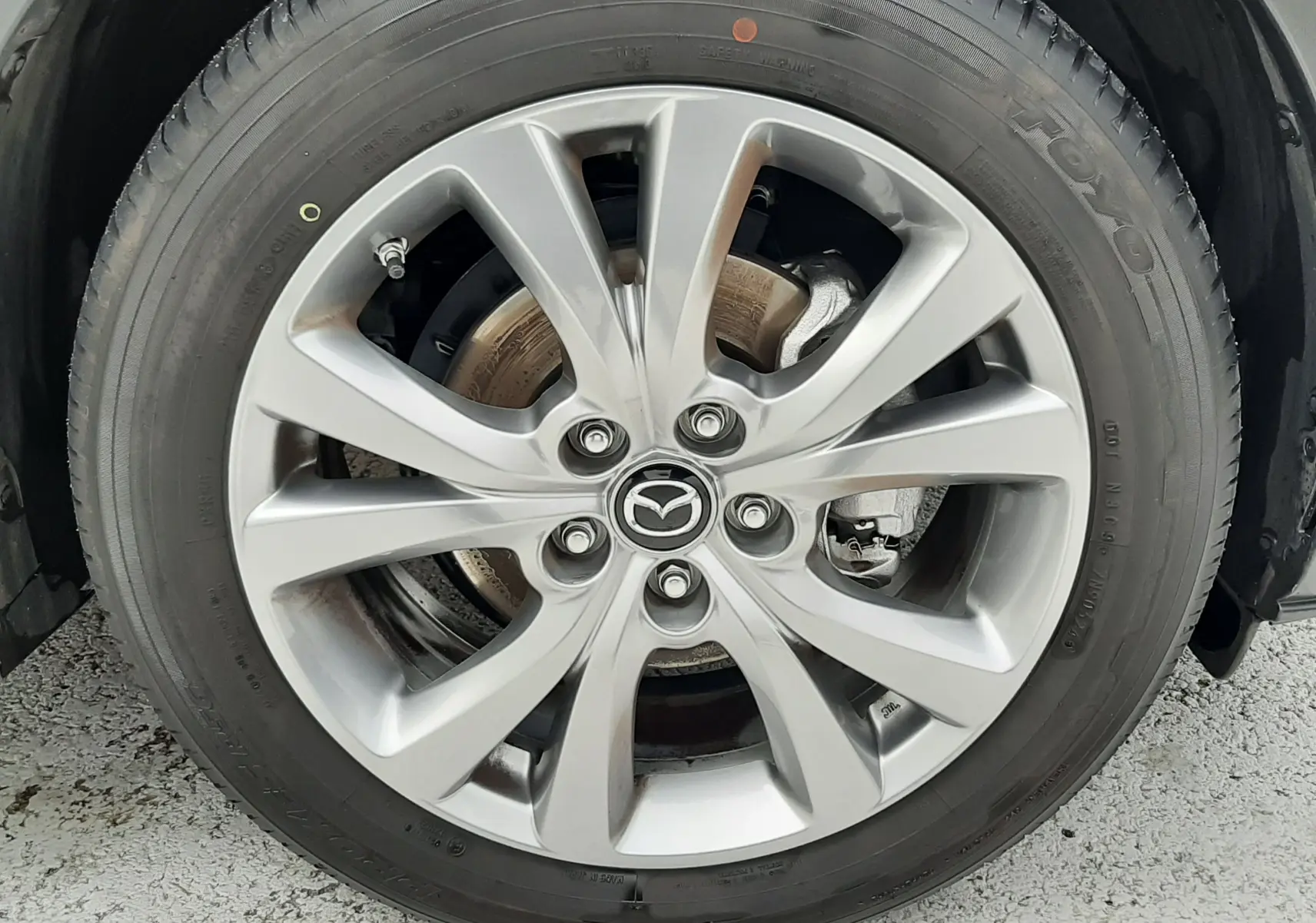 Gros plan sur la roue avant droite du Mazda CX-30 2024 en blanc céramique avec jante alliage 18 pouces et logo Mazda central.