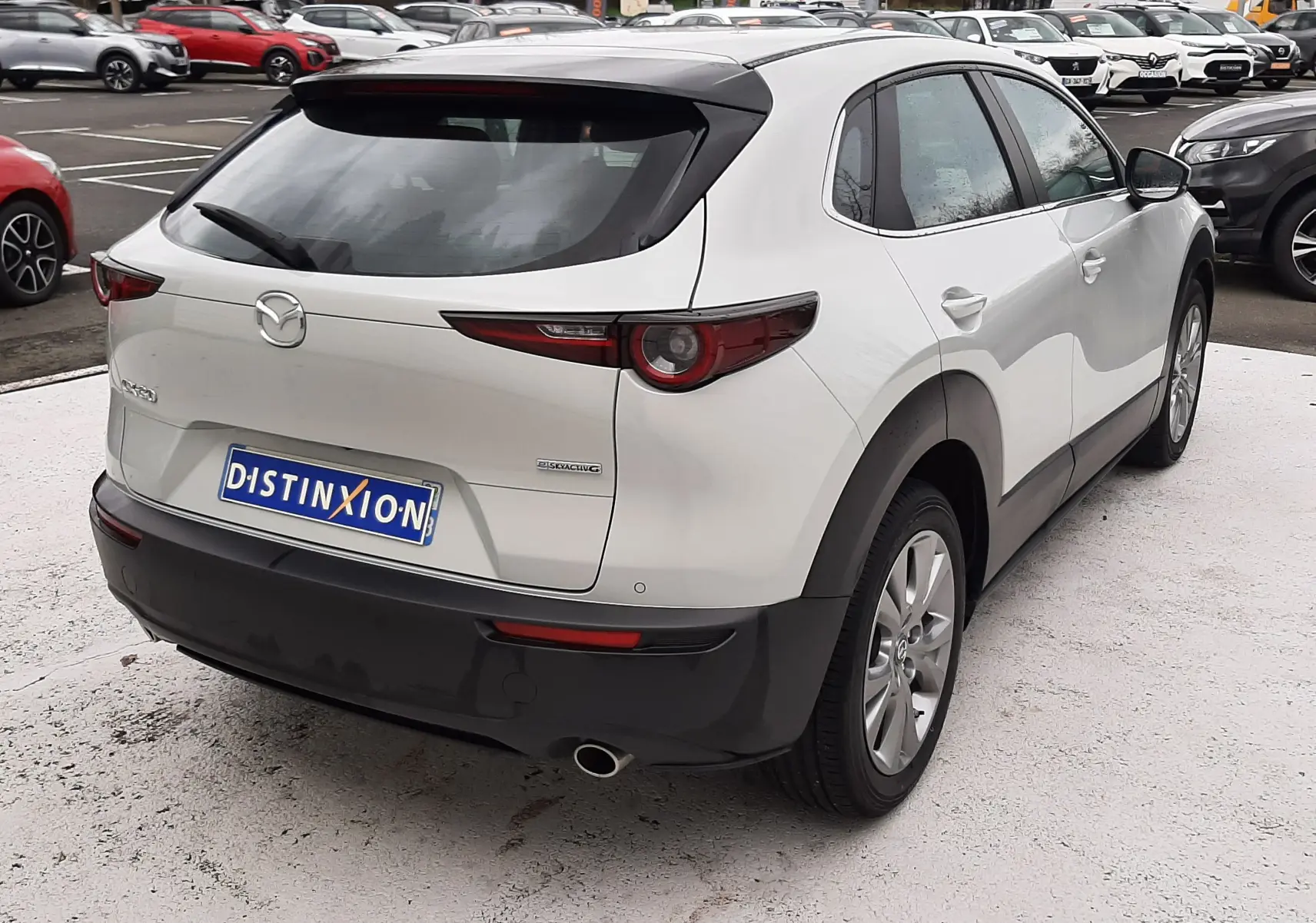 Vue 3/4 arrière droite d'un Mazda CX-30 2024 blanc céramique avec toit noir et feux arrière effilés.