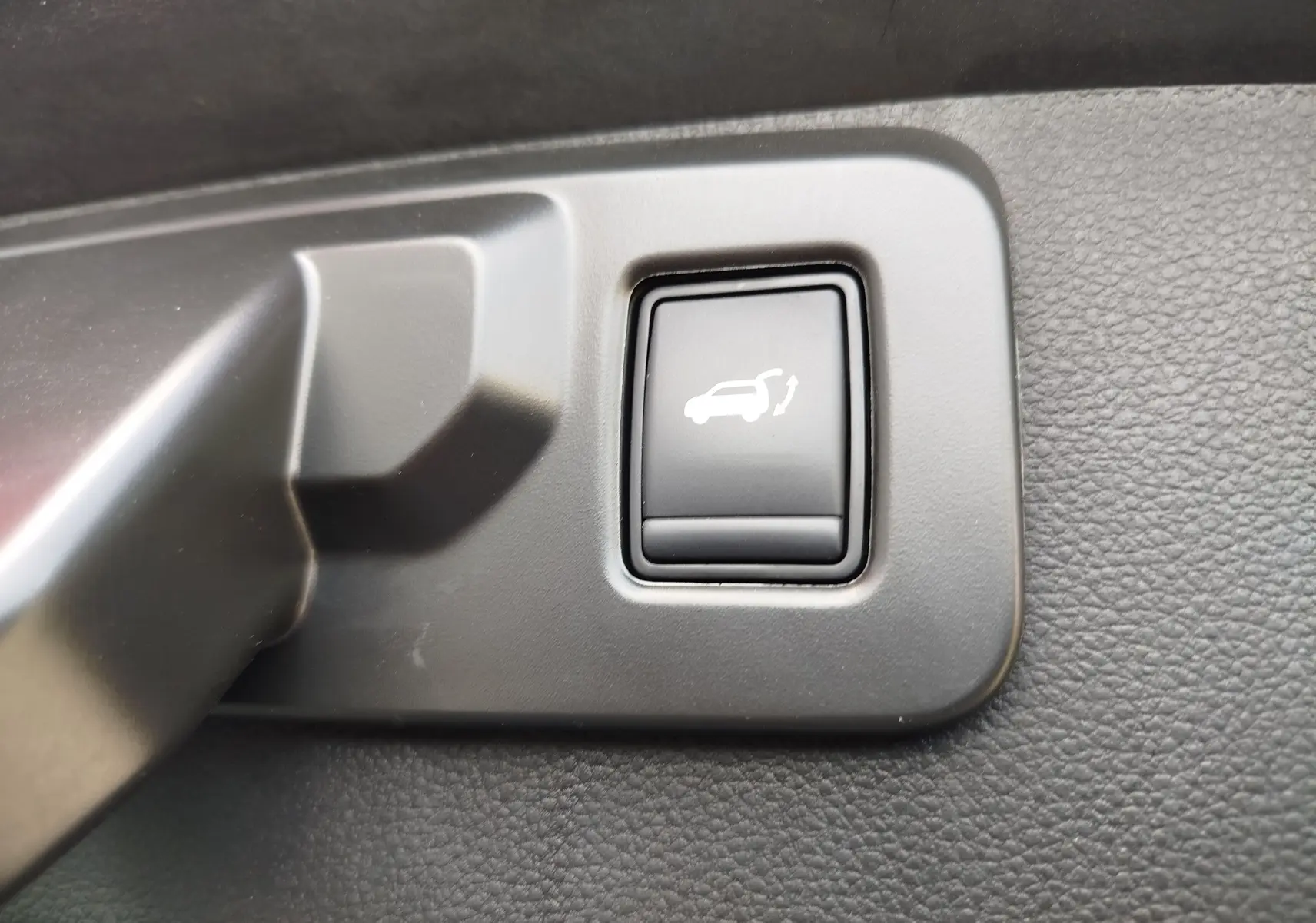 Bouton intérieur noir de déverrouillage du hayon sur panneau en plastique gris, détail de la Renault Symbioz 2025.