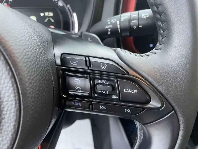Gros plan sur les commandes au volant côté droit d'une Toyota Aygo X rouge piment avec toit noir, montrant les boutons de régulateur et multimédia.