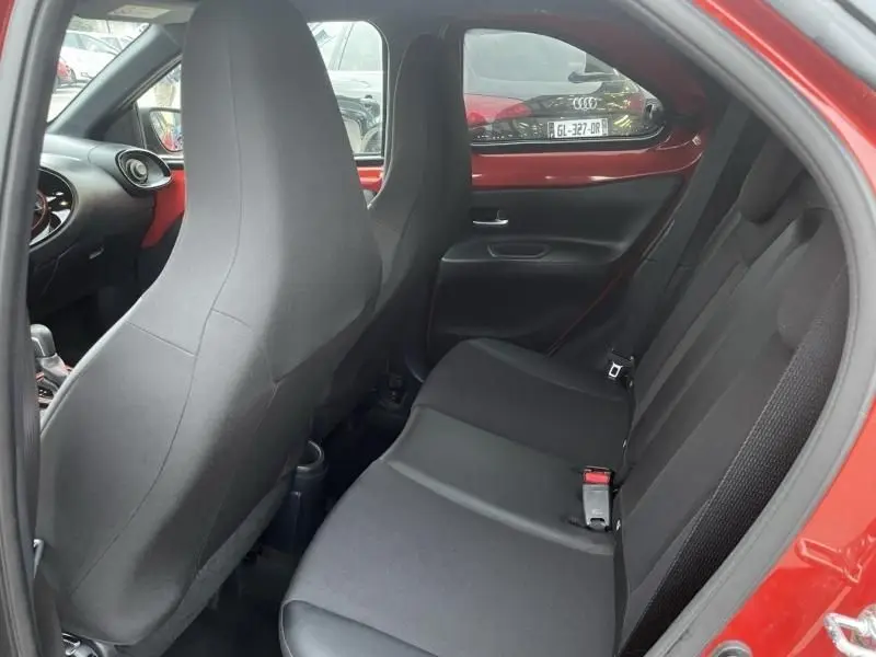 Vue intérieure côté droit de la banquette arrière noire et des sièges avant dans une Toyota Aygo X rouge piment avec toit noir.