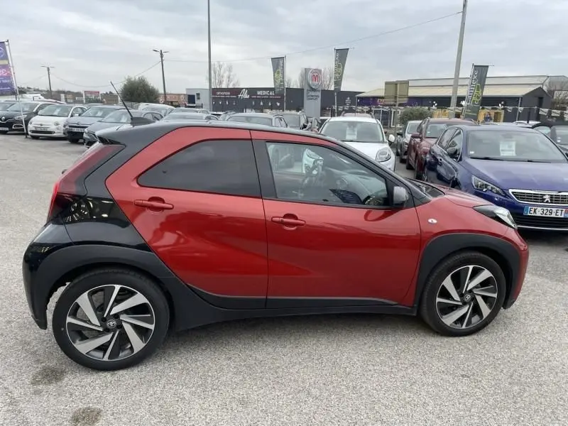 Vue de profil côté droit d'une Toyota Aygo X 2023 rouge piment avec toit noir et jantes alliage distinctives.