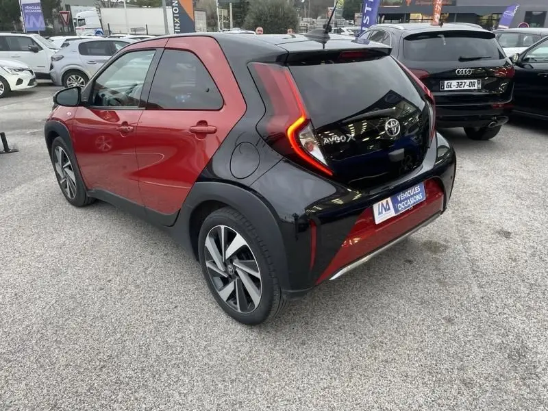 Vue 3/4 arrière droite de la Toyota Aygo X 2023 rouge piment avec toit noir et feux arrière en forme de C.