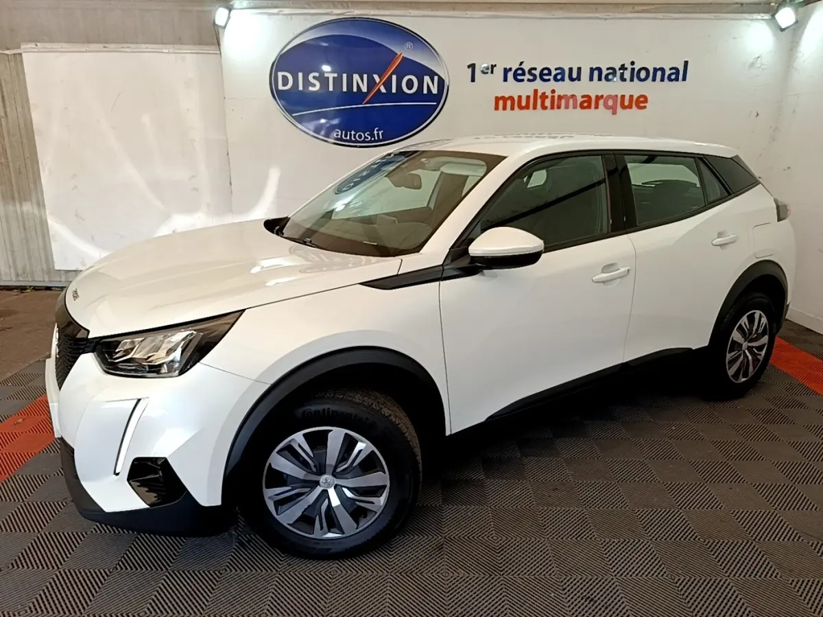 Peugeot 2008 blanc vue 3/4 avant droit, avec phares LED et jantes alliage, sur sol damier intérieur showroom.