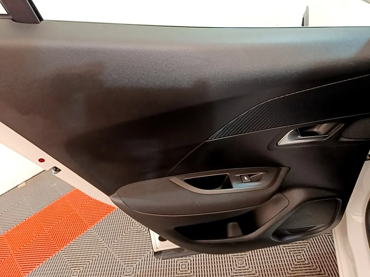 Vue rapprochée de la porte avant gauche noire d’un Peugeot 2008 blanc, avec poignée et commande de lève-vitre.