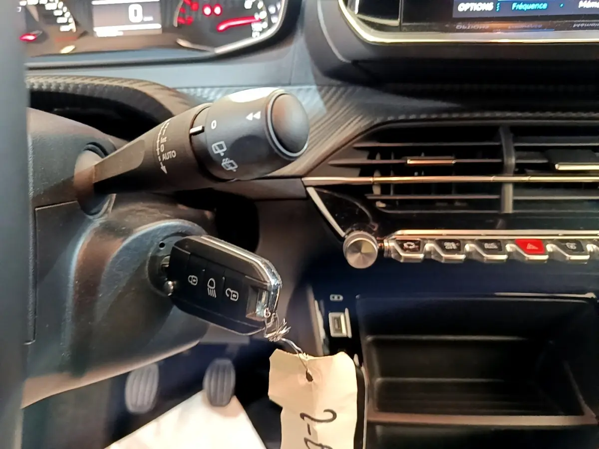 Gros plan intérieur sur le volant et la clé de contact d'une Peugeot 2008 1.5 BlueHDi, tableau de bord noir avec commandes argentées.