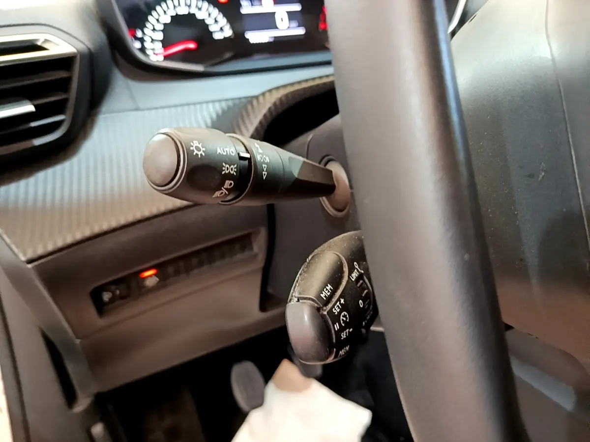 Gros plan sur la commande des phares et du régulateur de vitesse derrière le volant d’un Peugeot 2008 blanc.