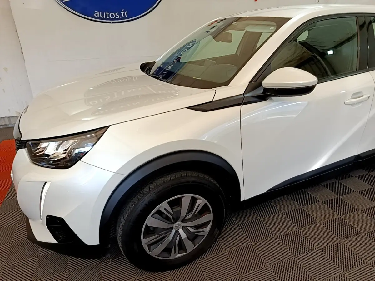 Vue 3/4 avant droit d'un Peugeot 2008 blanc avec jantes alliage et rétroviseur blanc sur fond intérieur.