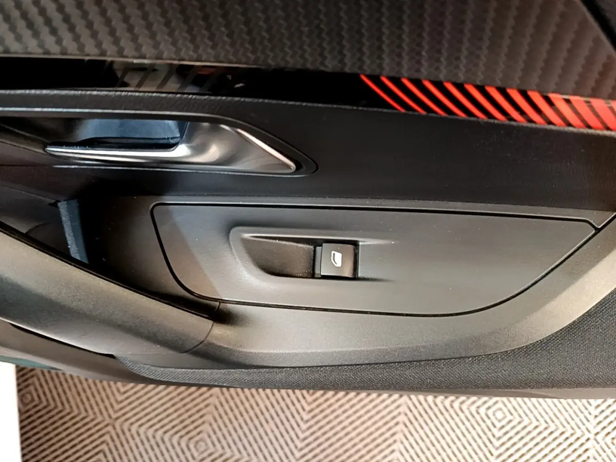 Détail de la porte côté conducteur d’une Peugeot 2008 blanche, avec bouton de commande de vitre et insert décoratif rouge.