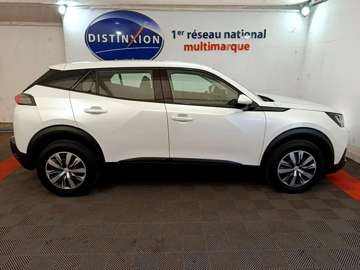 Vue de profil côté gauche d’un Peugeot 2008 blanc 2021, avec jantes alliage et toit noir contrasté en intérieur showroom.
