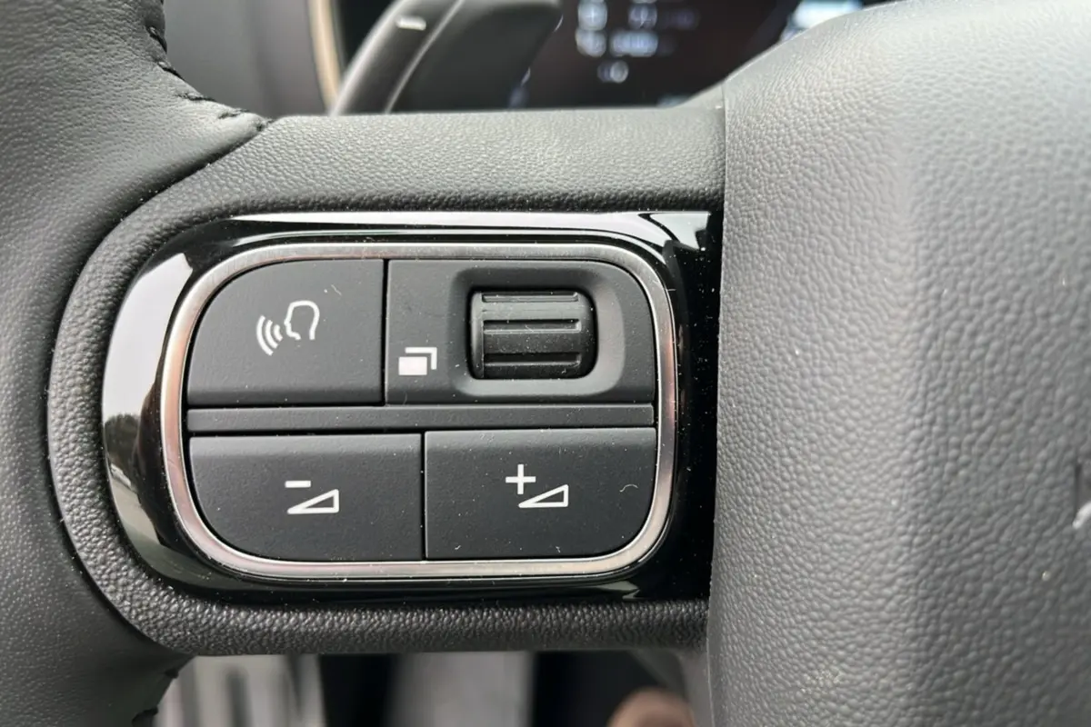 Gros plan sur les commandes multifonctions noires à gauche du volant cuir du Citroën C5 Aircross Hybrid Eclipse Blue 2025.