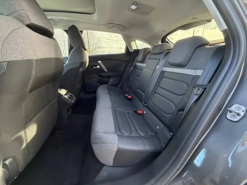 Vue intérieure arrière côté droit du Citroën C4 2024 gris, montrant les sièges bi-matière en tissu et cuir avec appuie-têtes intégrés.
