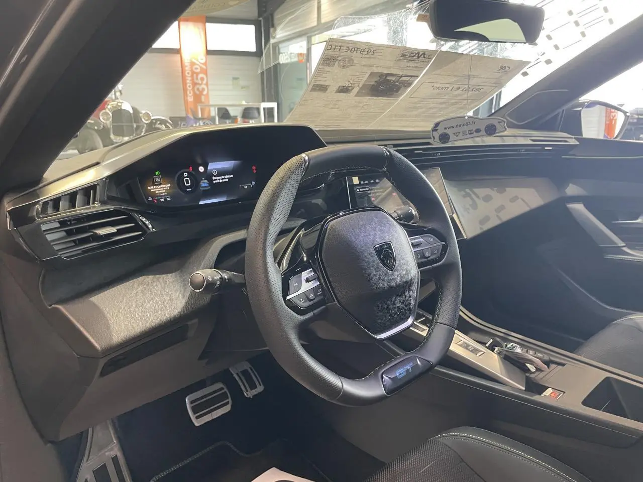 Vue intérieure du poste de conduite de la Peugeot 308 GT 2026, volant cuir GT avec surpiqûres vert Adamite et tableau de bord numérique.
