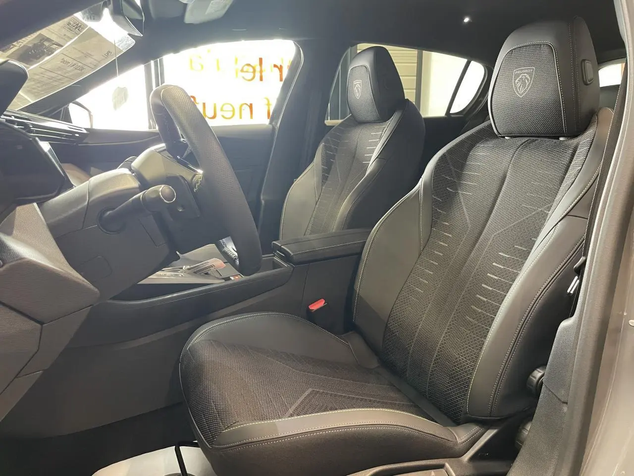 Vue intérieure côté conducteur de la Peugeot 308 gris selenium, sièges noirs avec logo Peugeot brodé sur appuie-tête.