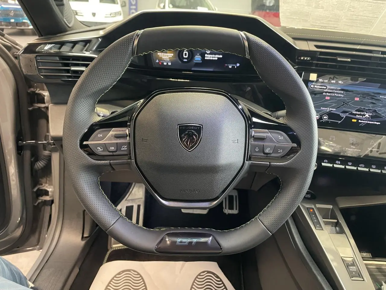 Volant compact GT en cuir noir avec logo Peugeot, vue de face sur tableau de bord numérique et console centrale.