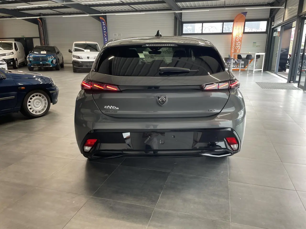 Vue arrière d'une Peugeot 308 GT gris Selenium avec feux arrière LED 3 griffes et jantes alliage en showroom.