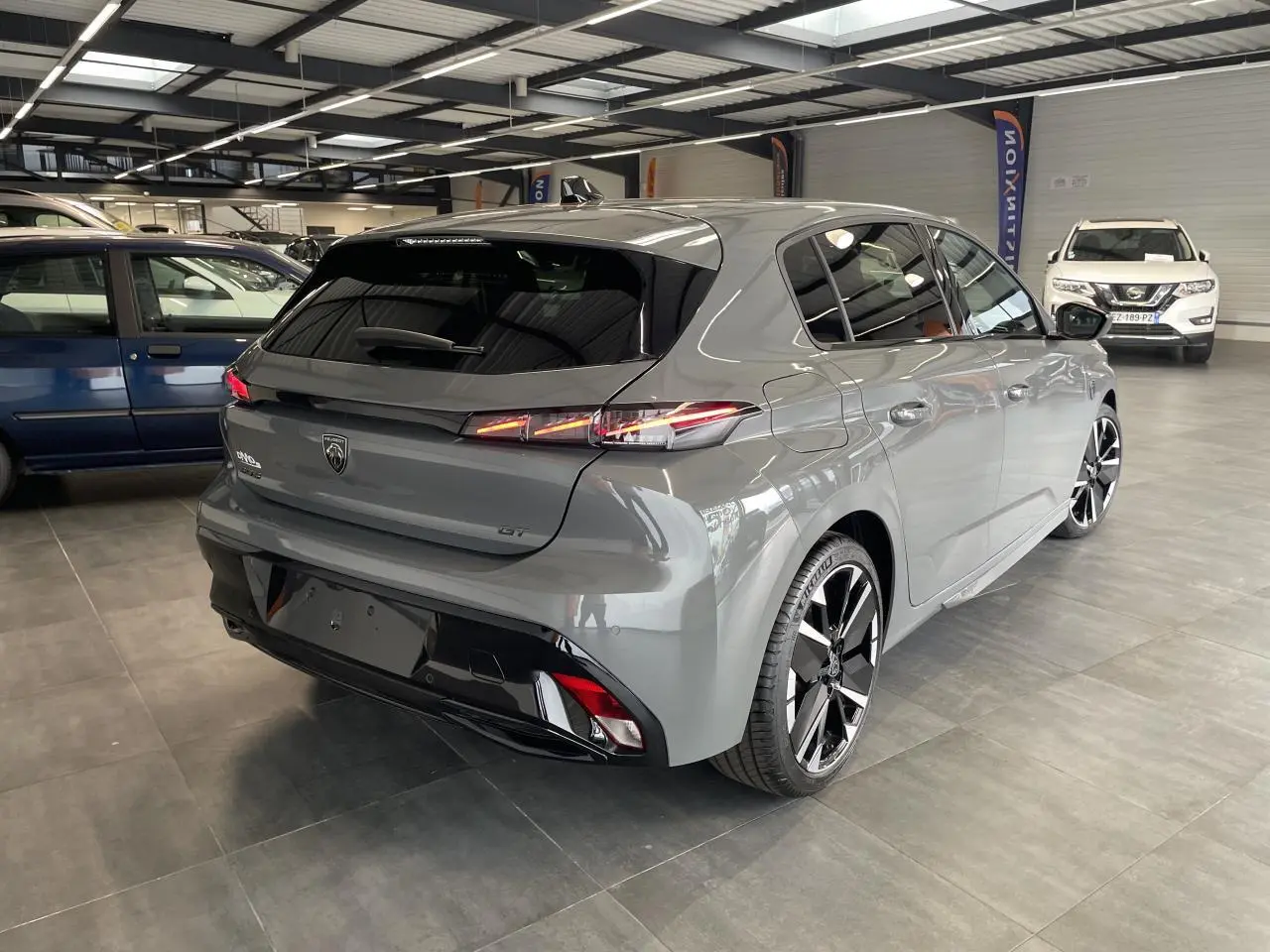 Peugeot 308 GT gris Selenium vue 3/4 arrière droit en intérieur, avec jantes alliage bi-tons et feux arrière LED griffés.