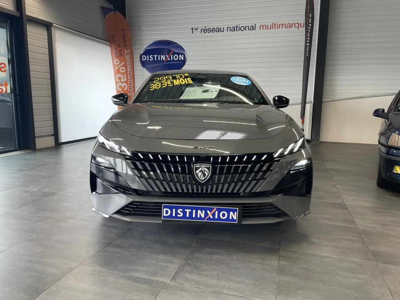 Vue frontale d'une Peugeot 308 gris selenium avec calandre noire brillante et logo lion lumineux en concession.